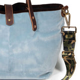 Close-up of the glacier blue velvet, brown velvet binding and brass D-ring with the olive leopard strap clipped on