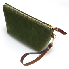 The Olive Velvet Travel Clutch, olive green velvet, shown with its detachable mahogany leather wristlet clipped to a brass D-ring