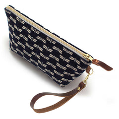 The Japanese Indigo Dragonflies Travel Clutch, white dragonflies on indigo, shown with its detachable mahogany leather wristlet clipped to a brass D-ring