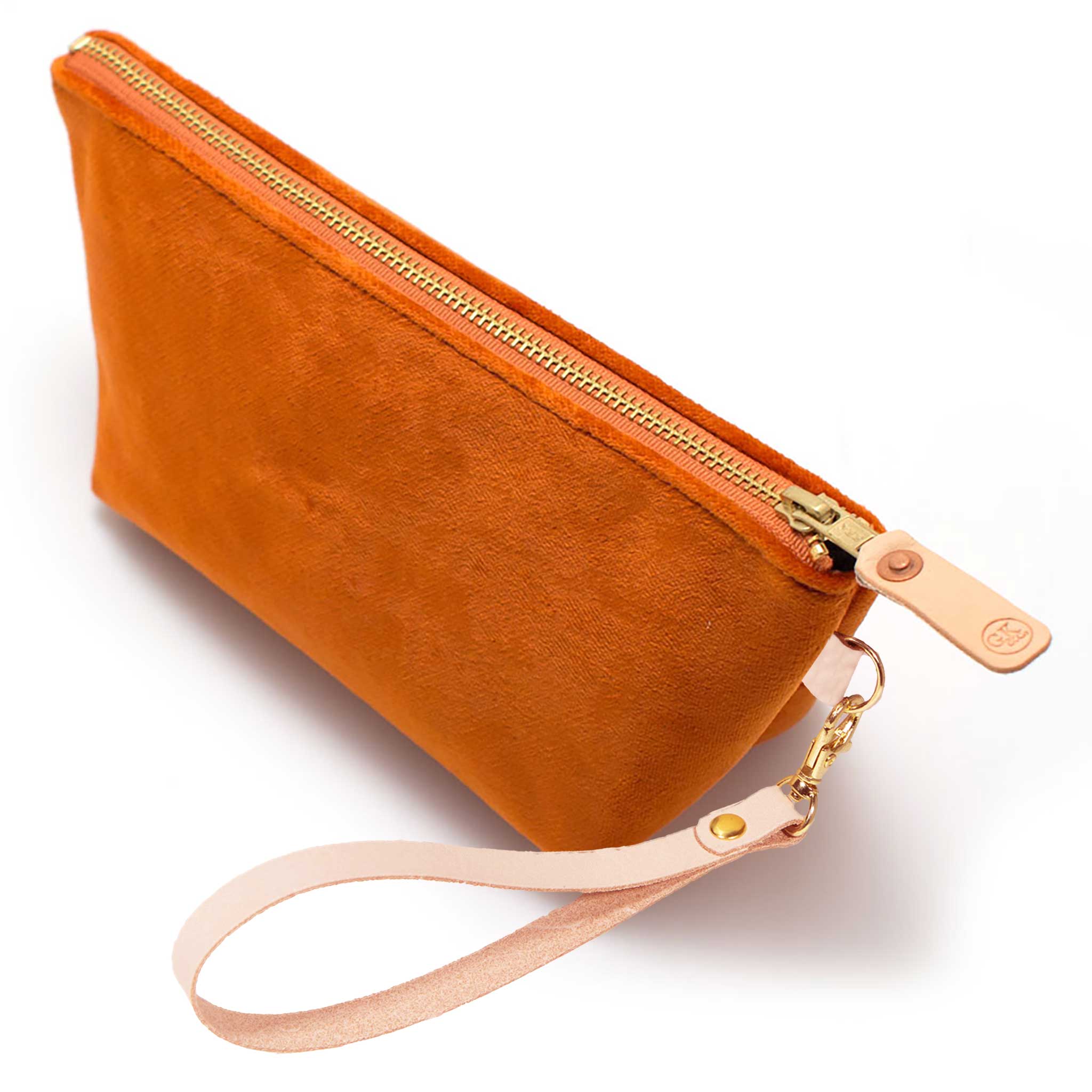 The Carrot Velvet Travel Clutch, carrot orange velvet, shown with its detachable blonde leather wristlet clipped to a brass D-ring