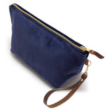 The Navy Velvet Travel Clutch, navy velvet, shown with its detachable mahogany leather wristlet clipped to a brass D-ring