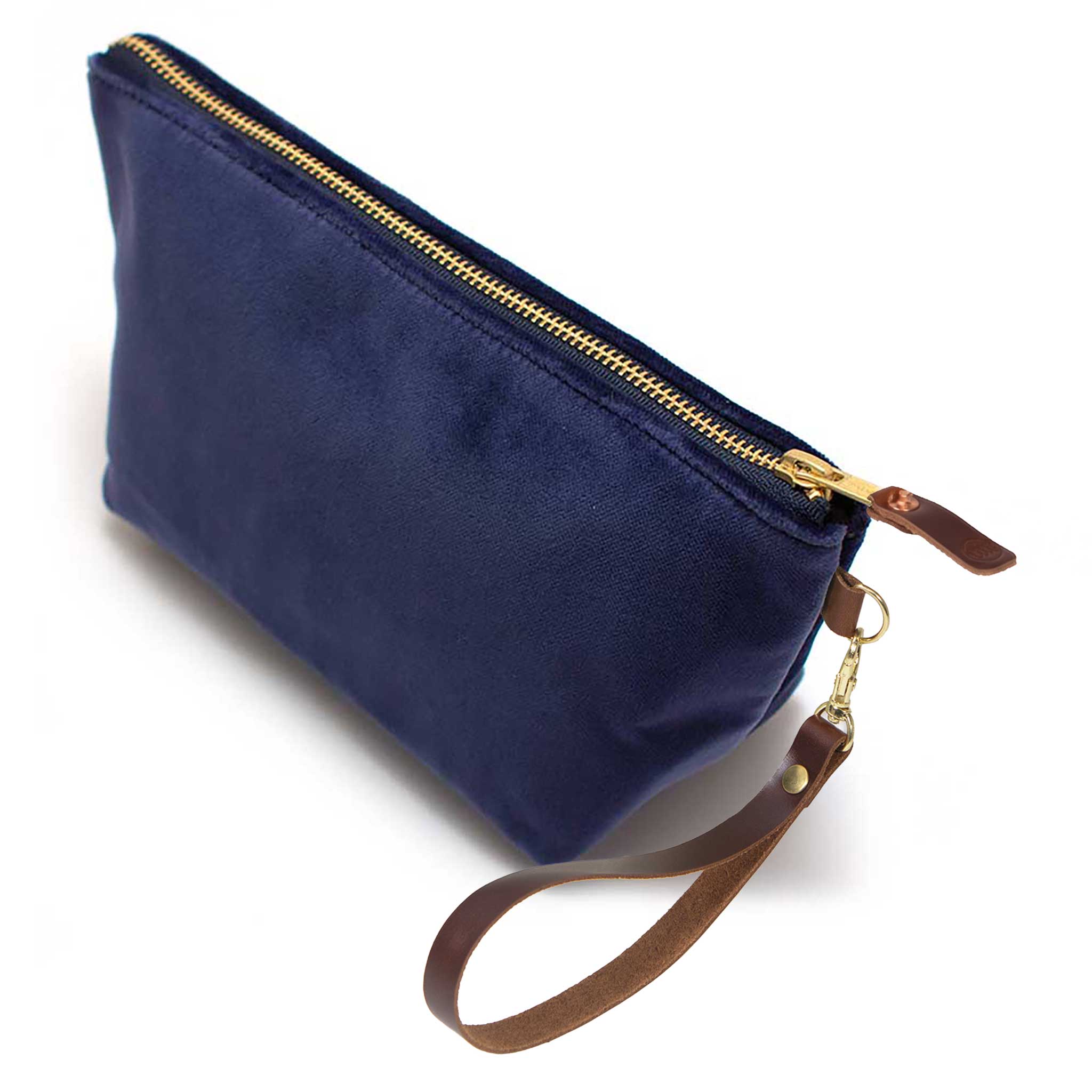 The Navy Velvet Travel Clutch, navy velvet, shown with its detachable mahogany leather wristlet clipped to a brass D-ring