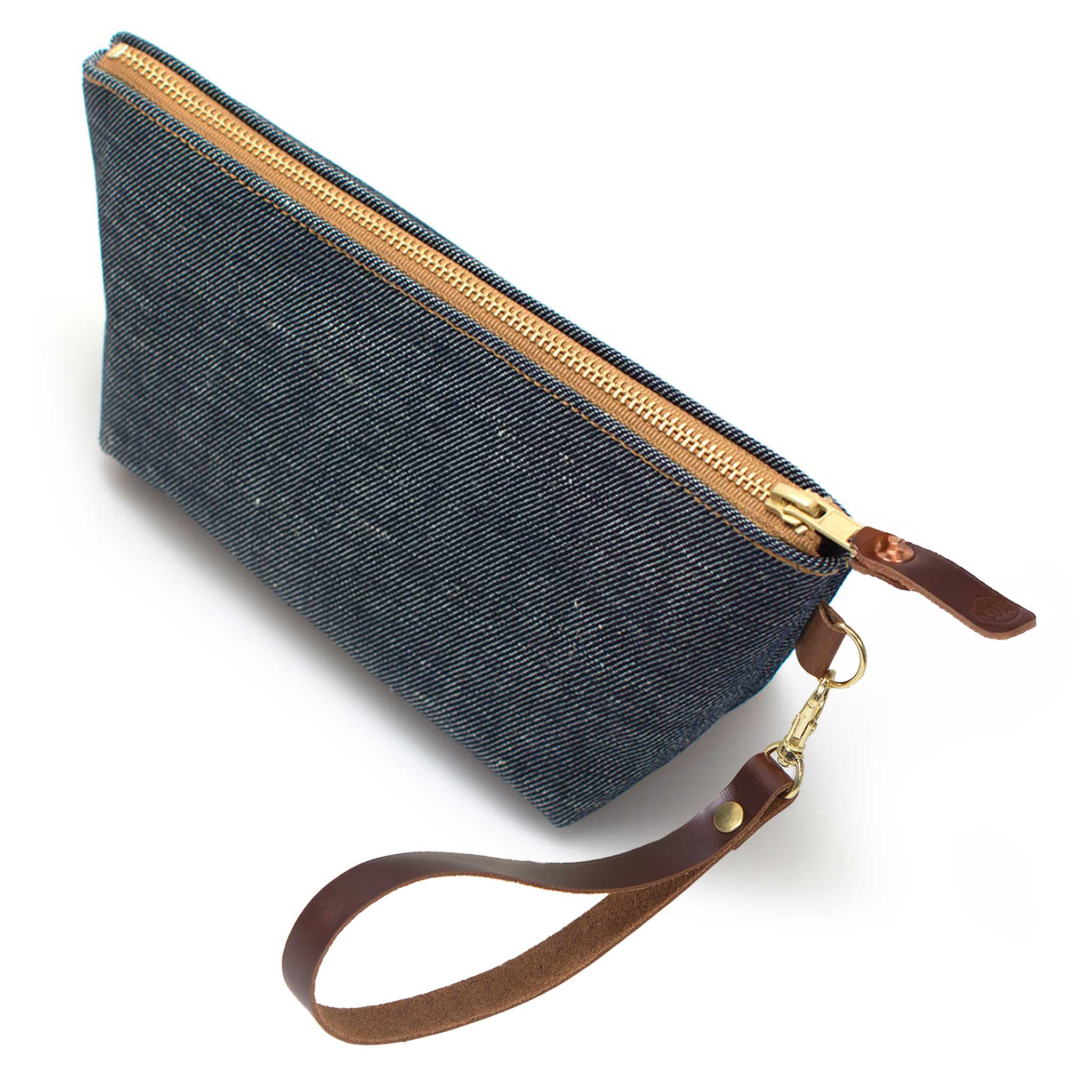 The Japanese Denim Travel Clutch, indigo denim, shown with its detachable mahogany leather wristlet clipped to a brass D-ring