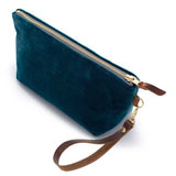 The Ocean Velvet Travel Clutch, ocean teal velvet, shown with its detachable mahogany leather wristlet clipped to a brass D-ring
