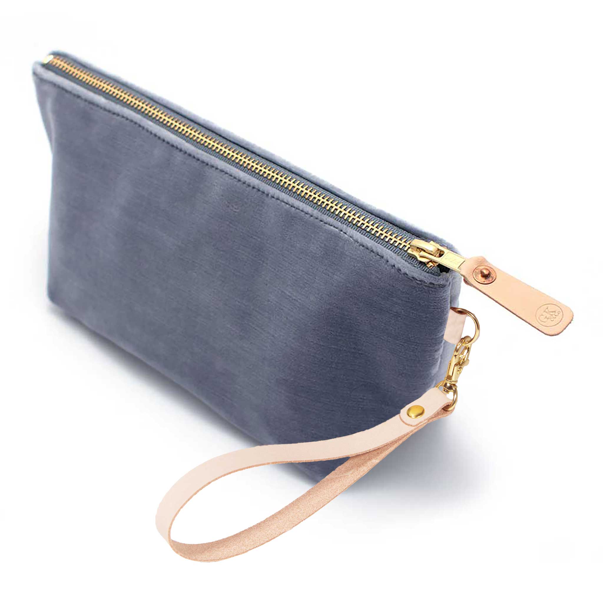 The Cloudy Velvet Travel Clutch, blue-grey velvet, shown with its detachable blonde leather wristlet clipped to a brass D-ring