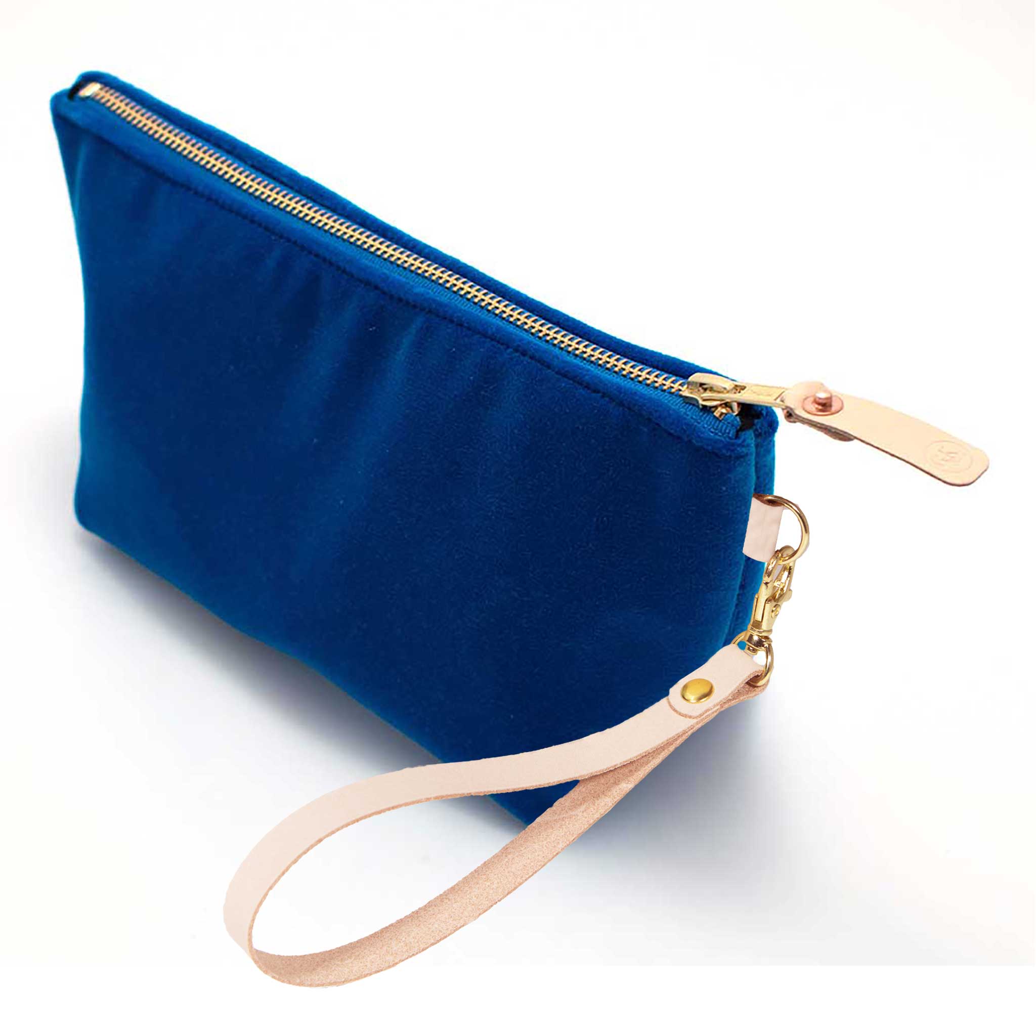 The Sapphire Velvet Travel Clutch, sapphire blue velvet, shown with its detachable blonde leather wristlet clipped to a brass D-ring