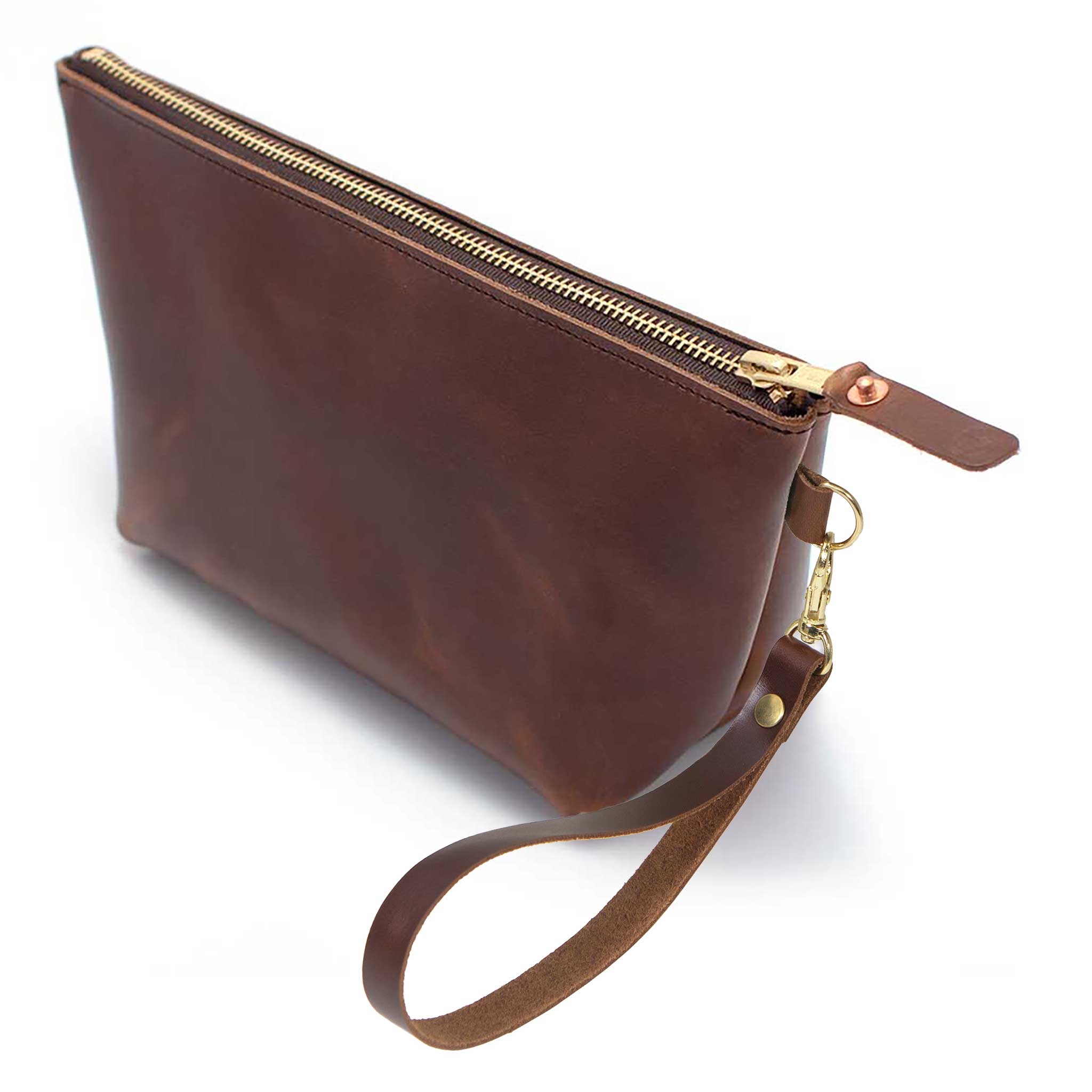 The Mahogany Leather Travel Clutch, brown leather, shown with its detachable mahogany leather wristlet clipped to a brass D-ring