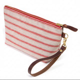 The Sailor Stripe Linen Travel Clutch, red stripes on flax linen, shown with its detachable mahogany leather wristlet clipped to a brass D-ring