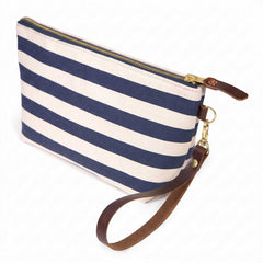The Navy Cabana Stripe Travel Clutch, wide navy and white stripes, shown with its detachable mahogany leather wristlet clipped to a brass D-ring