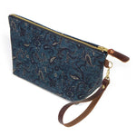 The Dark Indigo Paisley Travel Clutch, dark indigo paisley, shown with its detachable mahogany leather wristlet clipped to a brass D-ring