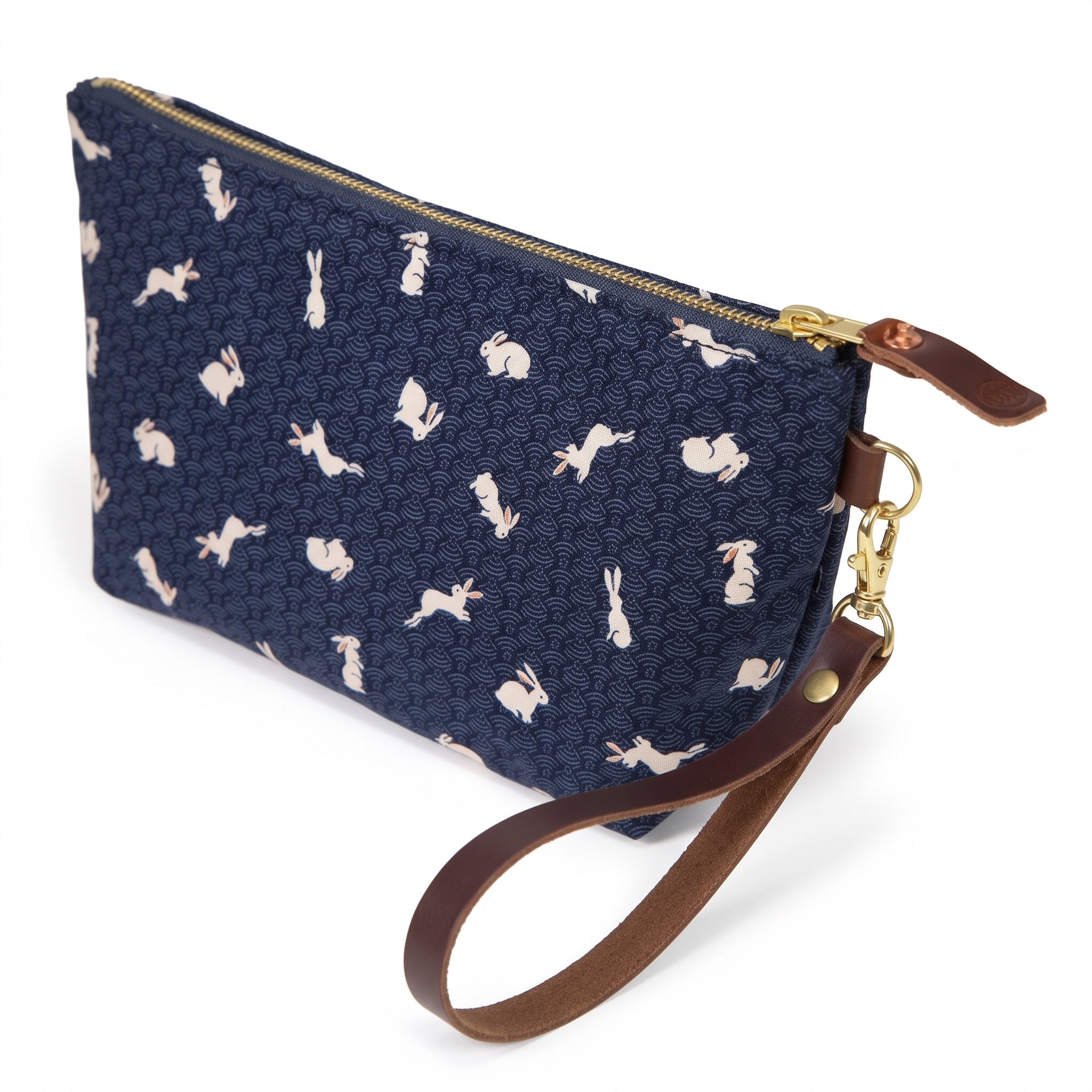 The Nousagi Japanese Indigo Travel Clutch, cream rabbits on navy, shown with its detachable mahogany leather wristlet clipped to a brass D-ring