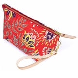 The French Country Floral Travel Clutch, blue and yellow blooms on red, shown with its detachable blonde leather wristlet clipped to a brass D-ring