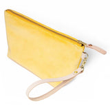 The Sunshine Velvet Travel Clutch, sunshine yellow velvet, shown with its detachable blonde leather wristlet clipped to a brass D-ring