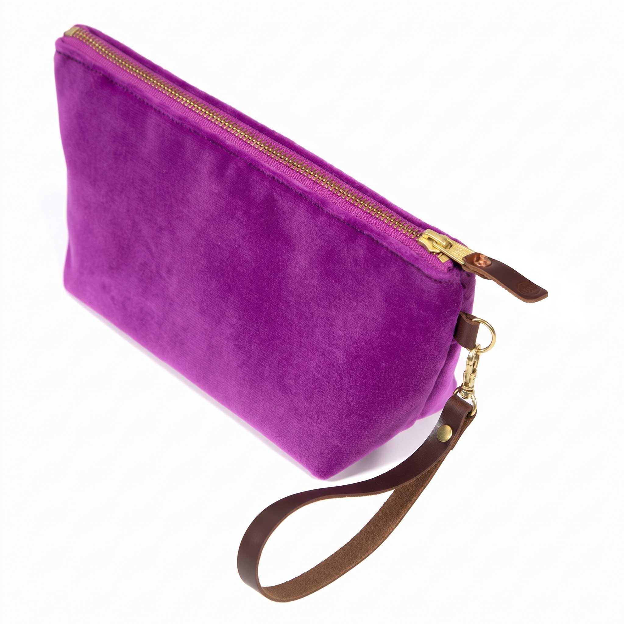 The Fuchsia Velvet Travel Clutch, fuchsia velvet, shown with its detachable mahogany leather wristlet clipped to a brass D-ring
