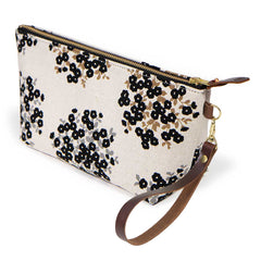 The Dots & Blooms Travel Clutch, black dots and blooms on cream, shown with its detachable mahogany leather wristlet clipped to a brass D-ring