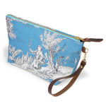 The Cerulean Toile Travel Clutch, white toile scenes on cerulean blue, shown with its detachable mahogany leather wristlet clipped to a brass D-ring