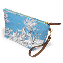 The Cerulean Toile Travel Clutch, white toile scenes on cerulean blue, shown with its detachable mahogany leather wristlet clipped to a brass D-ring