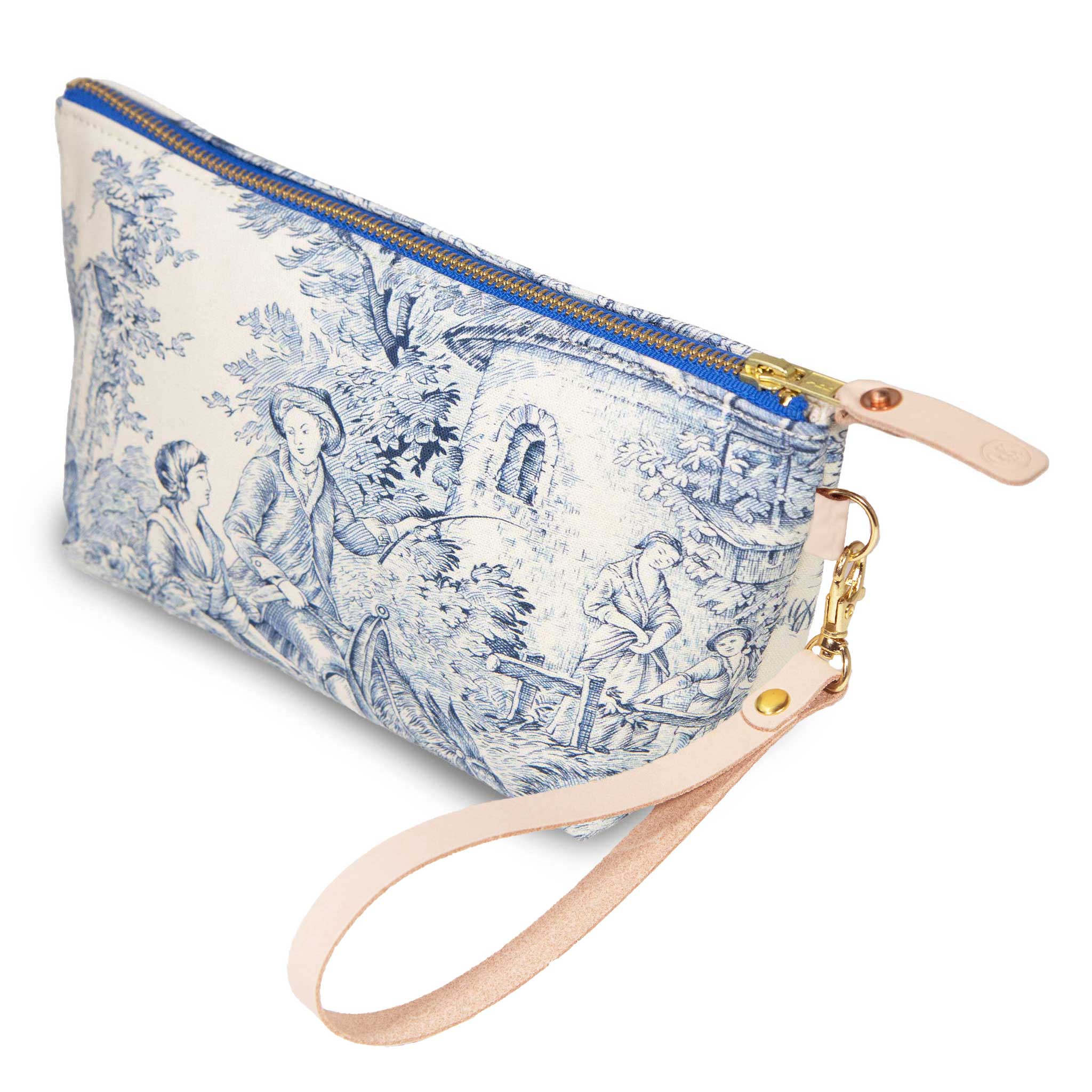 The Delftware Toile Travel Clutch, Delft blue toile on ivory, shown with its detachable blonde leather wristlet clipped to a brass D-ring